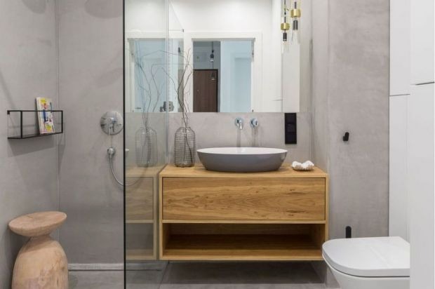 Nowoczesna łazienka z drewnianą szafką pod umywalką, szarą umywalką nablatową i minimalistycznym wystrojem. Widoczna kabina prysznicowa i toaleta.