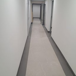 Creative-BUD Dmytro Semysiuk - Wykończony korytarz biurowy z jasnymi ścianami, szarą podłogą z płytek i nowoczesnym oświetleniem LED. Widok w perspektywie, ukazujący czystość i minimalizm wnętrza.