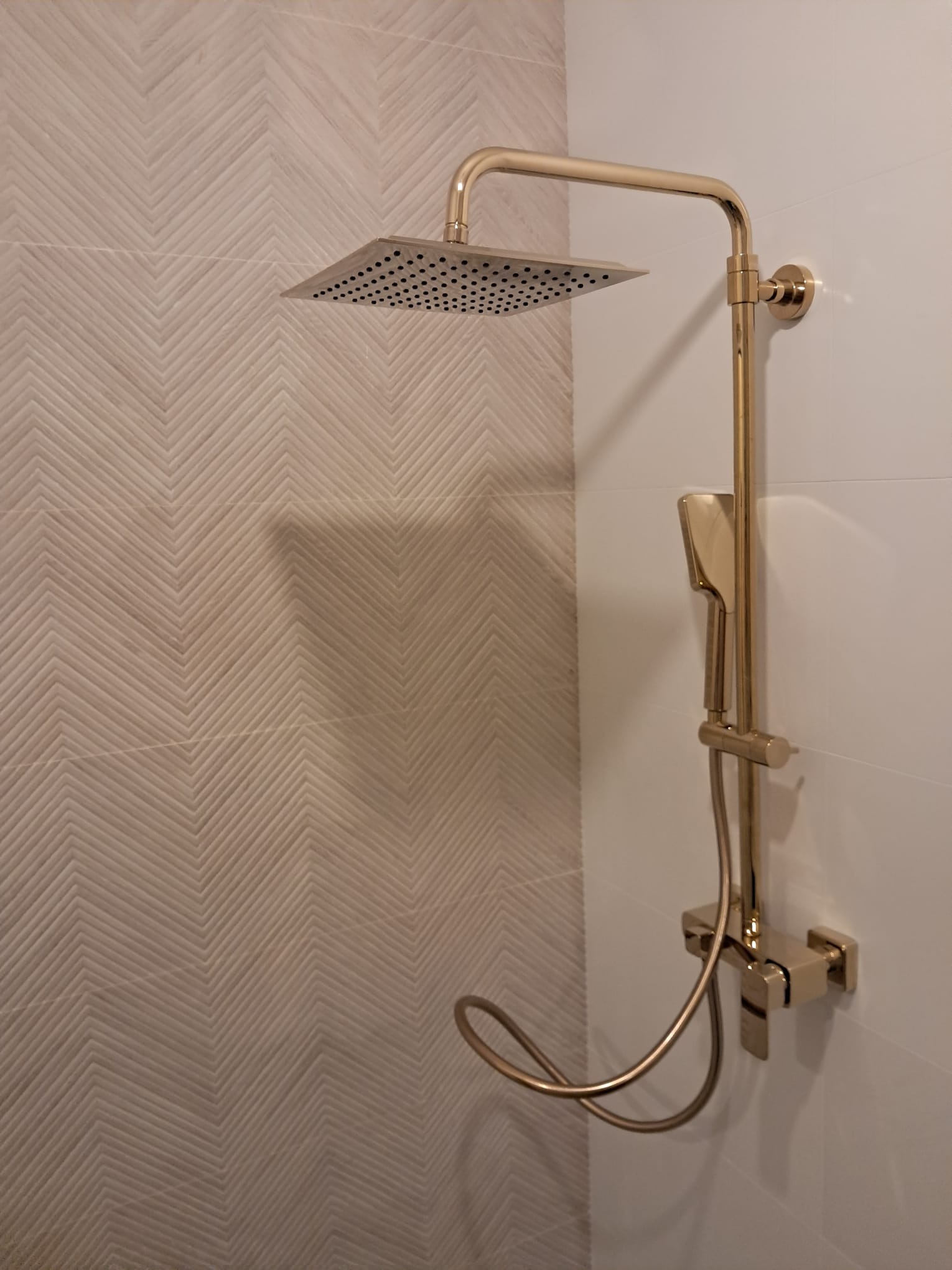 Złota armatura natryskowa na tle ściany z płytek w jodełkę. Nowoczesny design kabiny prysznicowej, eleganckie wykończenie. Detal wykończenia łazienki.