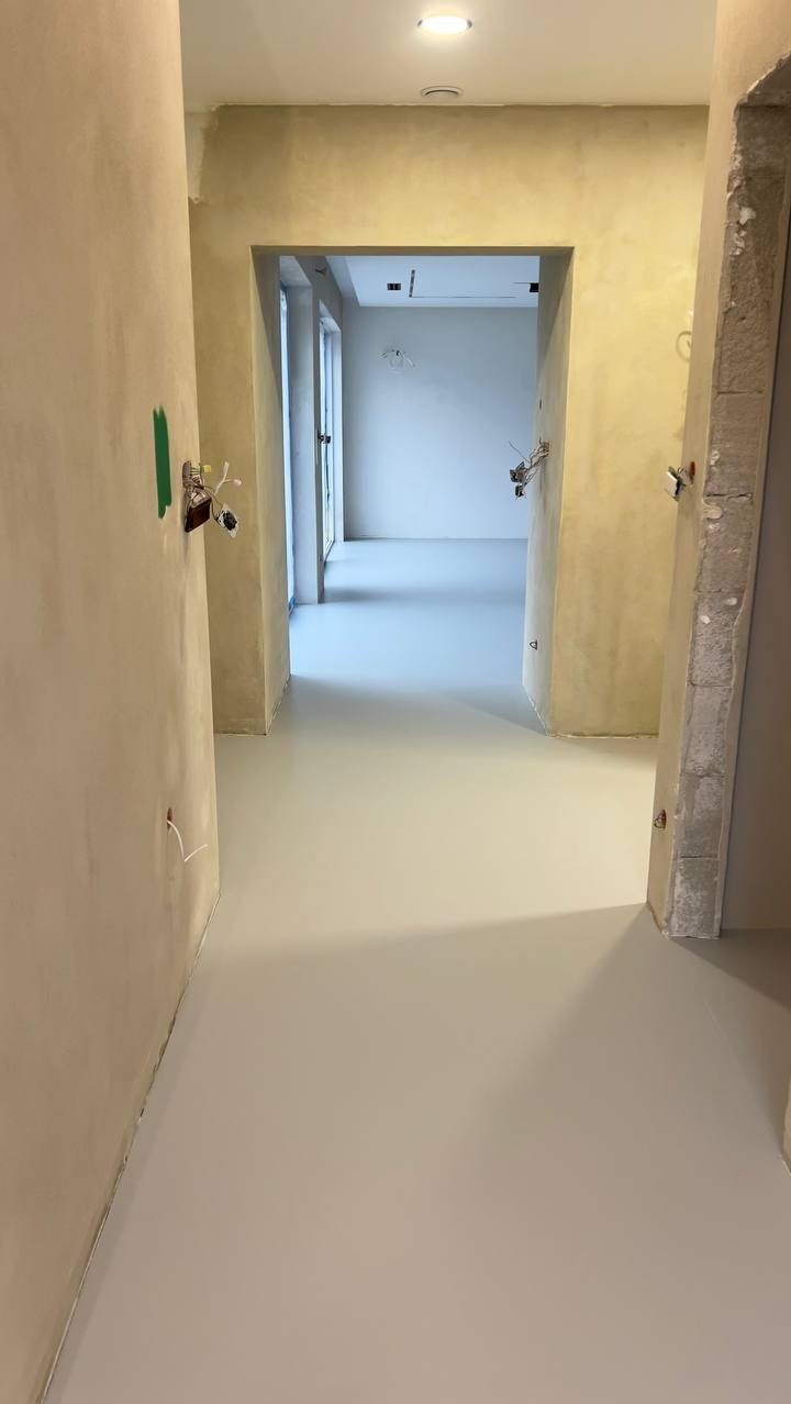Jasna, gładka posadzka w korytarzu w trakcie remontu. Widoczne niedokończone ściany i instalacje elektryczne. Minimalistyczny design, świeżo wylana podłoga.