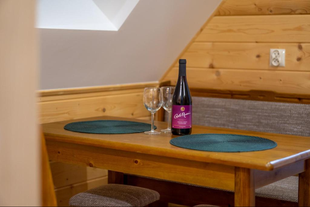 Drewniany stół w pokoju na poddaszu z butelką wina Carlo Rossi i dwoma kieliszkami, nakryty okrągłymi, zielonymi podkładkami. Przytulne wnętrze, gotowe na relaks.