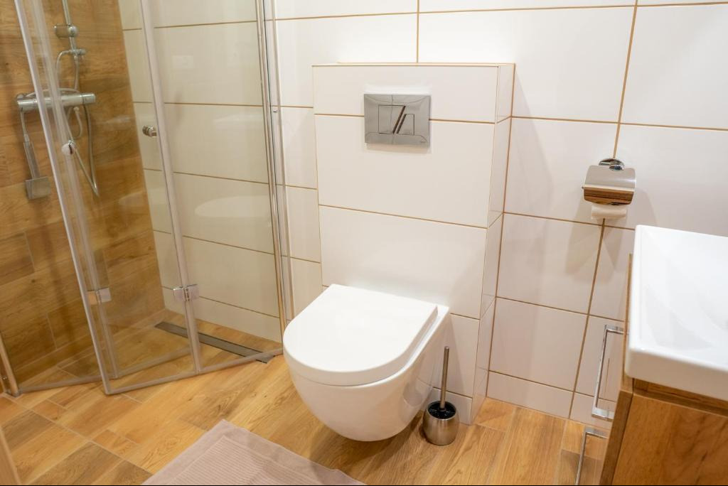 Nowoczesna łazienka z kabiną prysznicową i podwieszaną toaletą w Nowym Targu. Jasne płytki i drewnopodobne panele podłogowe.