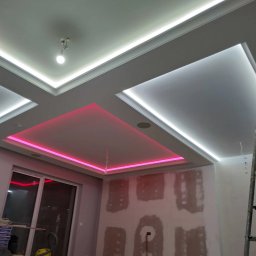 VLADLEN HRYBACHOV - Sufit podwieszany z oświetleniem LED: białe listwy i różowe kwadraty. Ściany w trakcie szpachlowania, widoczna drabina i odkurzacz. Nowoczesne wykończenie wnętrza.
