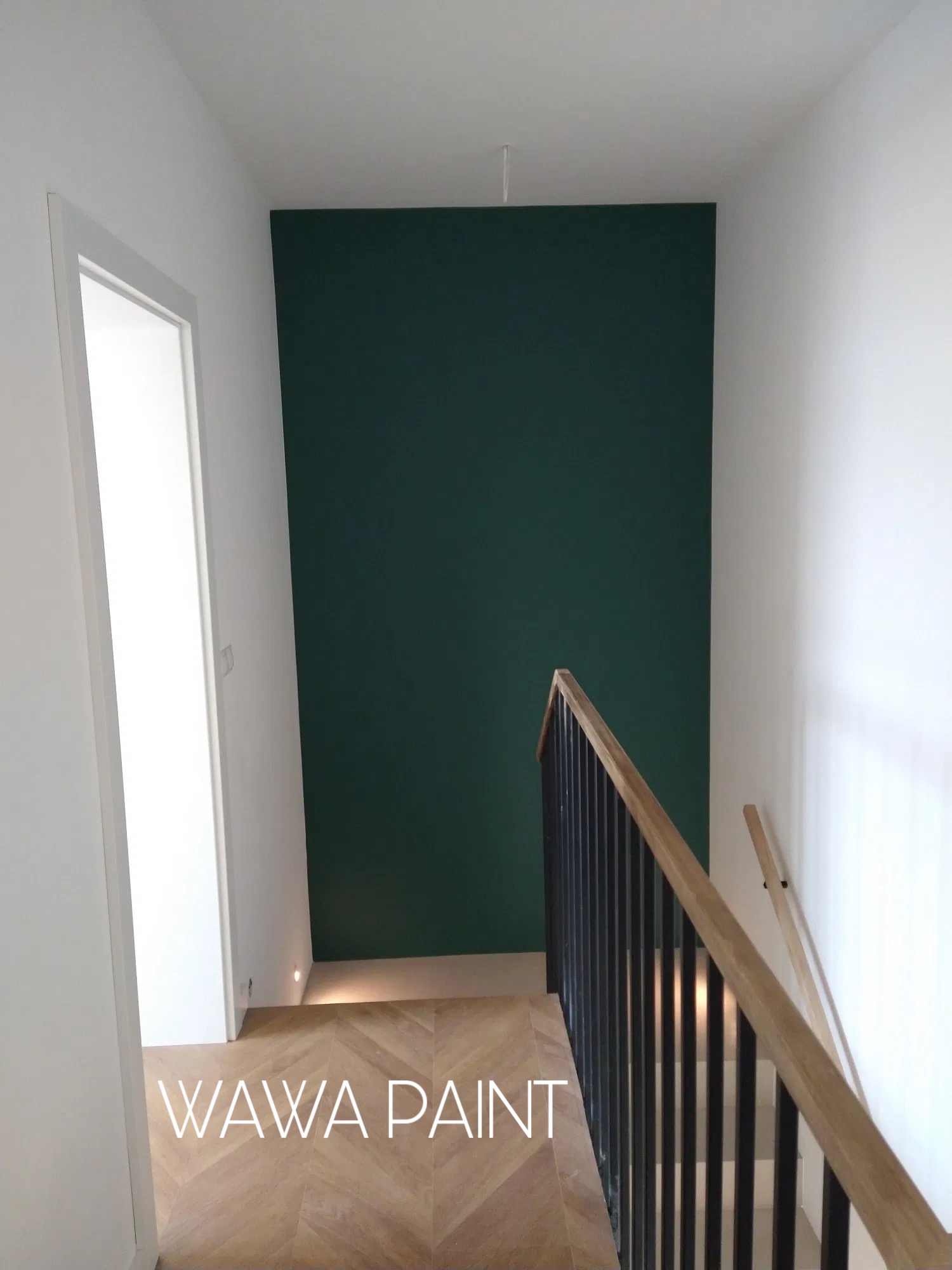 Klatka schodowa po malowaniu: ściana w odcieniu butelkowej zieleni kontrastuje z bielą ścian i stolarki. Parkiet ułożony we wzór jodełki. Balustrada z drewnianym pochwytem.