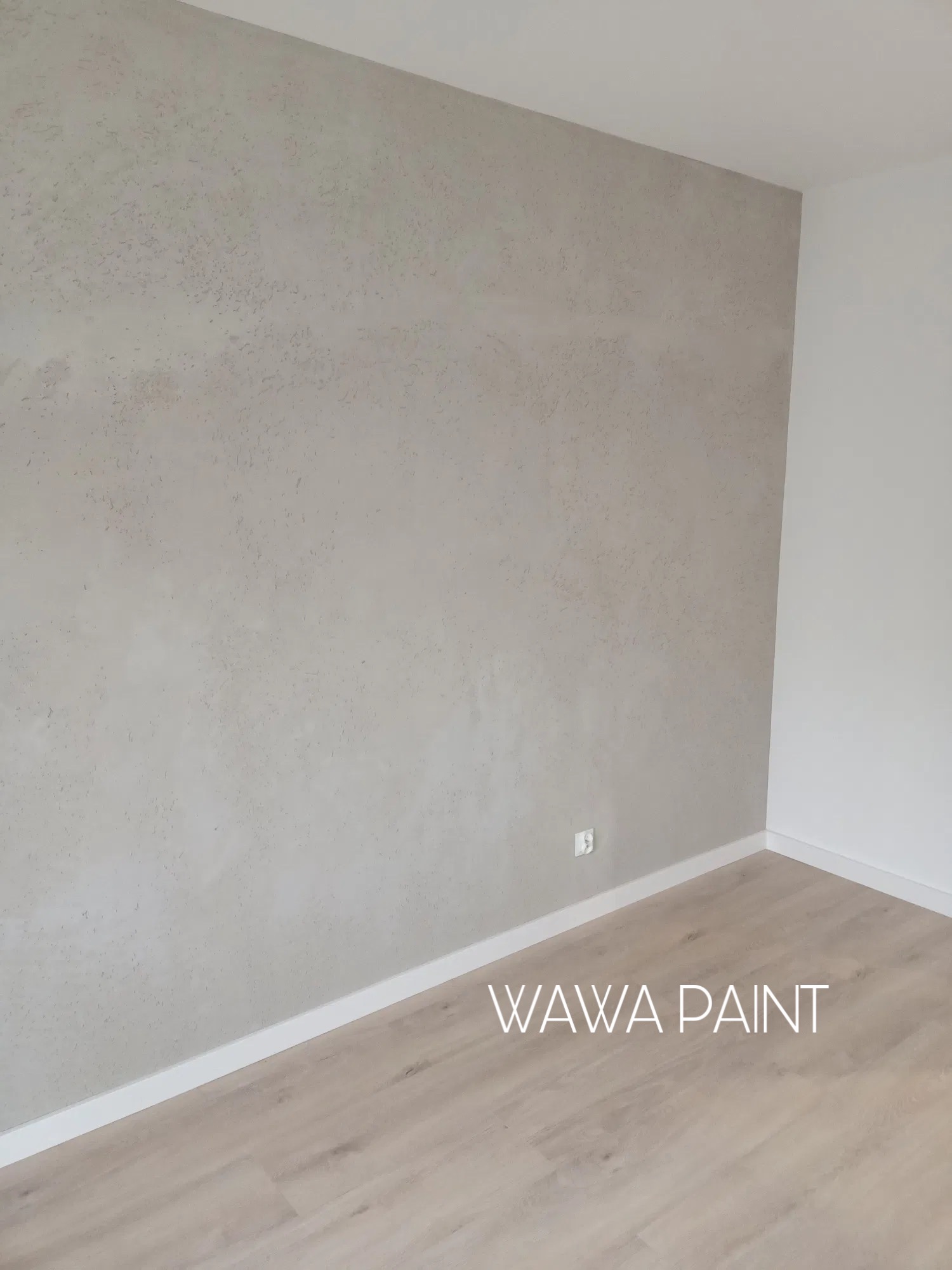 Wykończone wnętrze: ściana z dekoracyjną, beżową fakturą, biała listwa przypodłogowa i jasna podłoga. Widoczny fragment gniazdka elektrycznego.