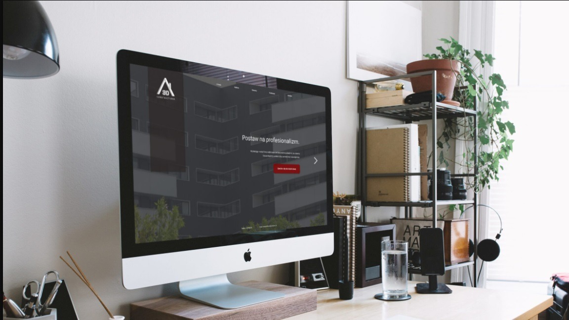 Ekran iMac prezentuje stronę internetową z minimalistycznym logo i hasłem 'Postaw na profesjonalizm', na biurku z roślinami i elementami dekoracyjnymi.