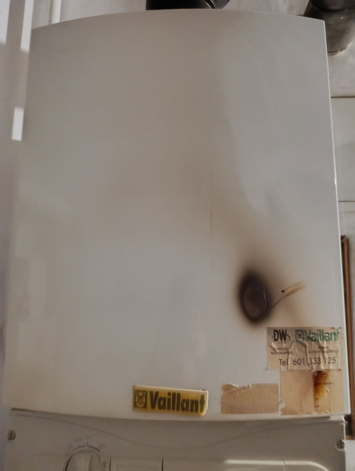 Biały piec gazowy Vaillant z widocznymi śladami okopcenia i naklejkami informacyjnymi. Widoczne uszkodzenia termiczne na obudowie pieca.