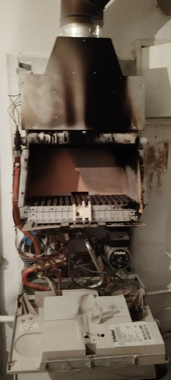 Otwarty, zabrudzony piec gazowy Vaillant w Kiekrz. Widoczne elementy wewnętrzne, ślady sadzy na obudowie i przewodach. Detaliczny widok wnętrza kotła.