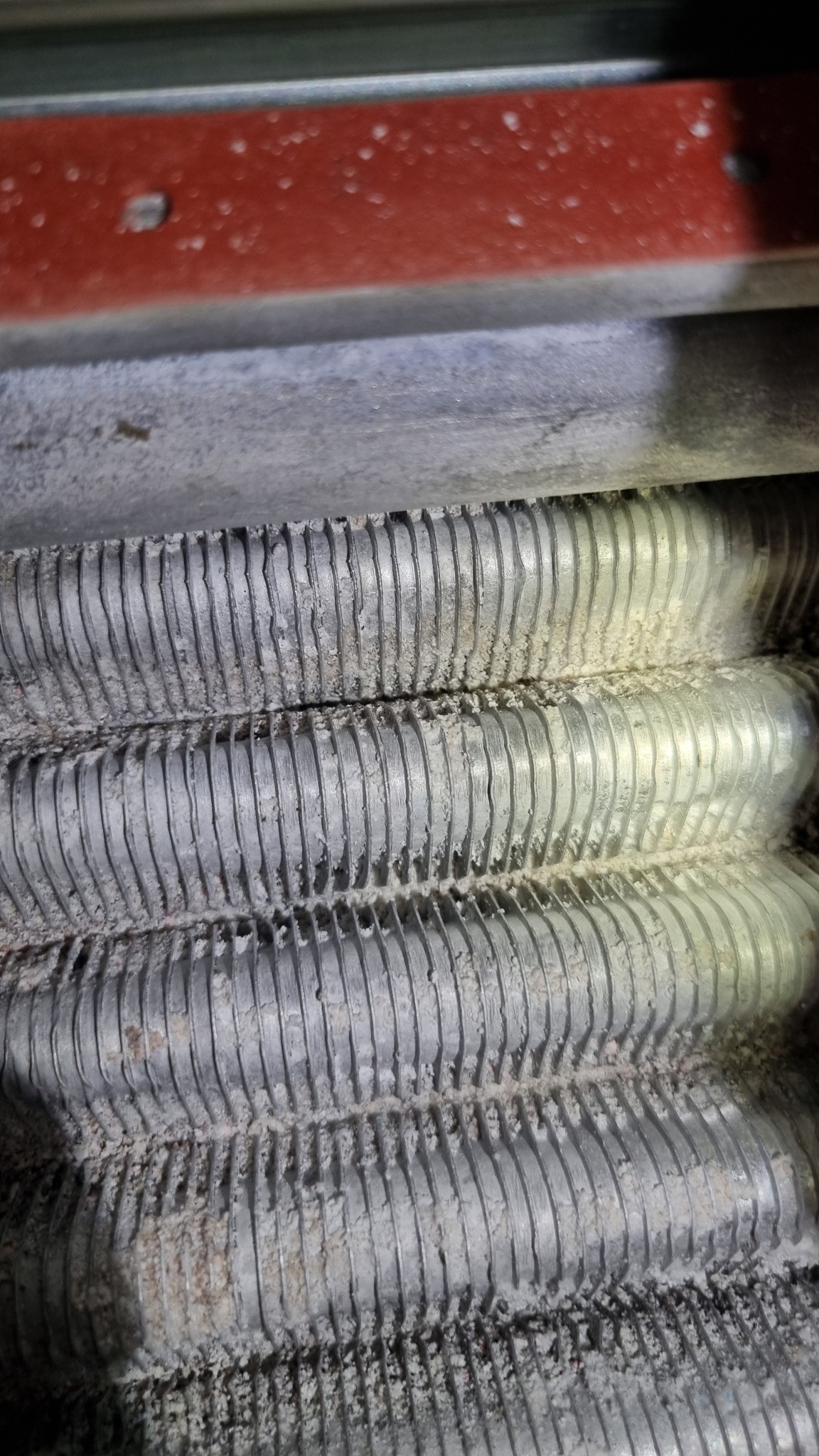 Żebrowany wymiennik ciepła pieca gazowego, pokryty białym osadem, widoczny z bliska pod kątem. Element instalacji grzewczej w trakcie przeglądu.