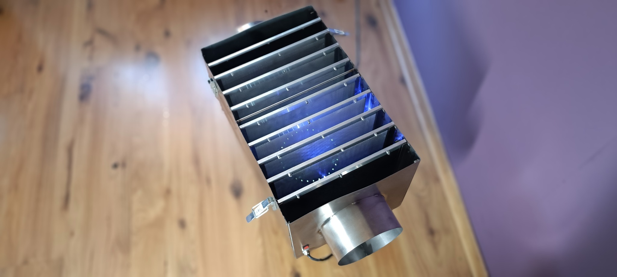 Lampa owadobójcza UV z metalową obudową na drewnianym blacie, widoczna niebieska poświata wewnątrz urządzenia.