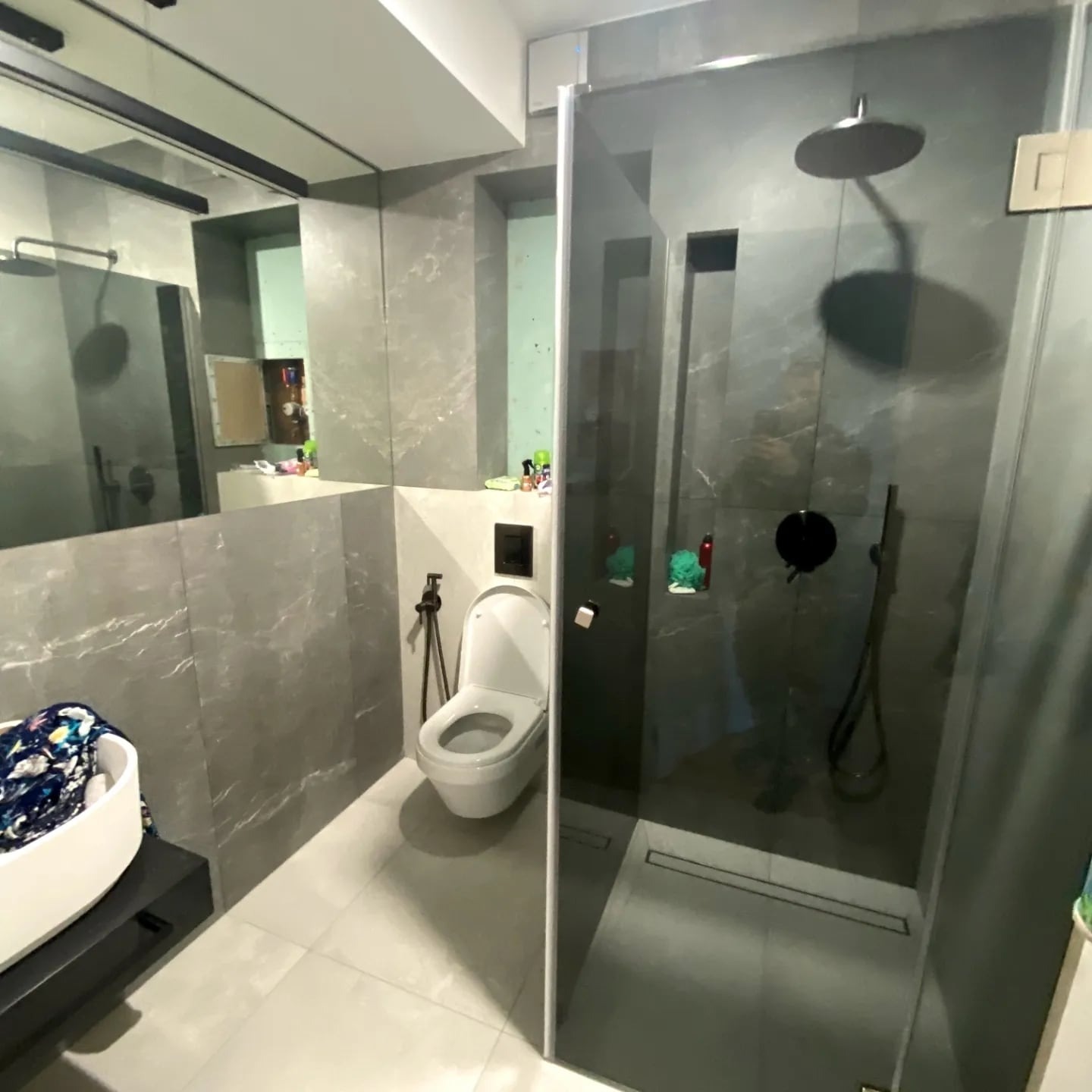 Nowoczesna łazienka z szarymi płytkami imitującymi marmur, kabiną prysznicową typu walk-in i podwieszaną toaletą. Umywalka nablatowa w rogu kadru.