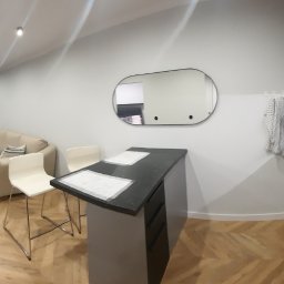 DOMINIK KAHL CRACOW LOCAL TOURS No.1 - Panoramiczne ujęcie nowoczesnego wnętrza: salon z aneksem kuchennym, parkiet w jodełkę, minimalistyczne meble, czarne blaty i owalne lustro. Jasne ściany, punktowe oświetlenie.