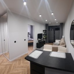 DOMINIK KAHL CRACOW LOCAL TOURS No.1 - Nowoczesne wnętrze mieszkania z parkietem w jodełkę, widokiem na salon i sypialnię, oraz dużym, asymetrycznym lustrem na ścianie. Minimalistyczny design.