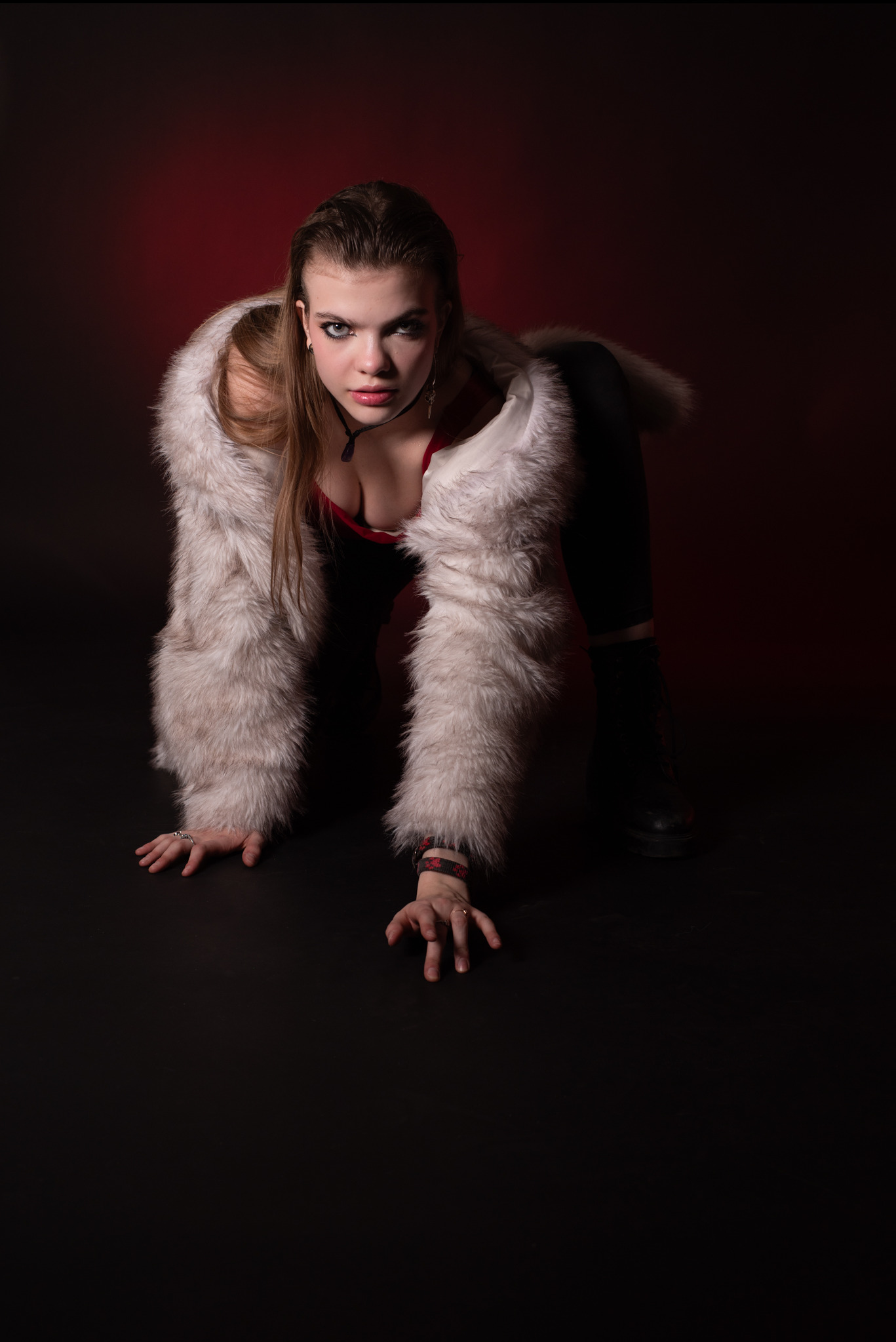 Kobieta w futrze pozuje na czarnym tle z czerwonym akcentem, patrząc wprost w obiektyw. Ujęcie z dołu podkreśla jej spojrzenie i stylizację.