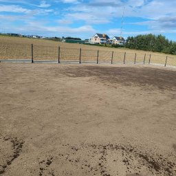 BRUK-BUD JANUSZ KWIDZIŃSKI - Nowoczesne ogrodzenie panelowe z podmurówką na wyrównanym terenie. W tle domy jednorodzinne i błękitne niebo z chmurami. Widok z poziomu gruntu.