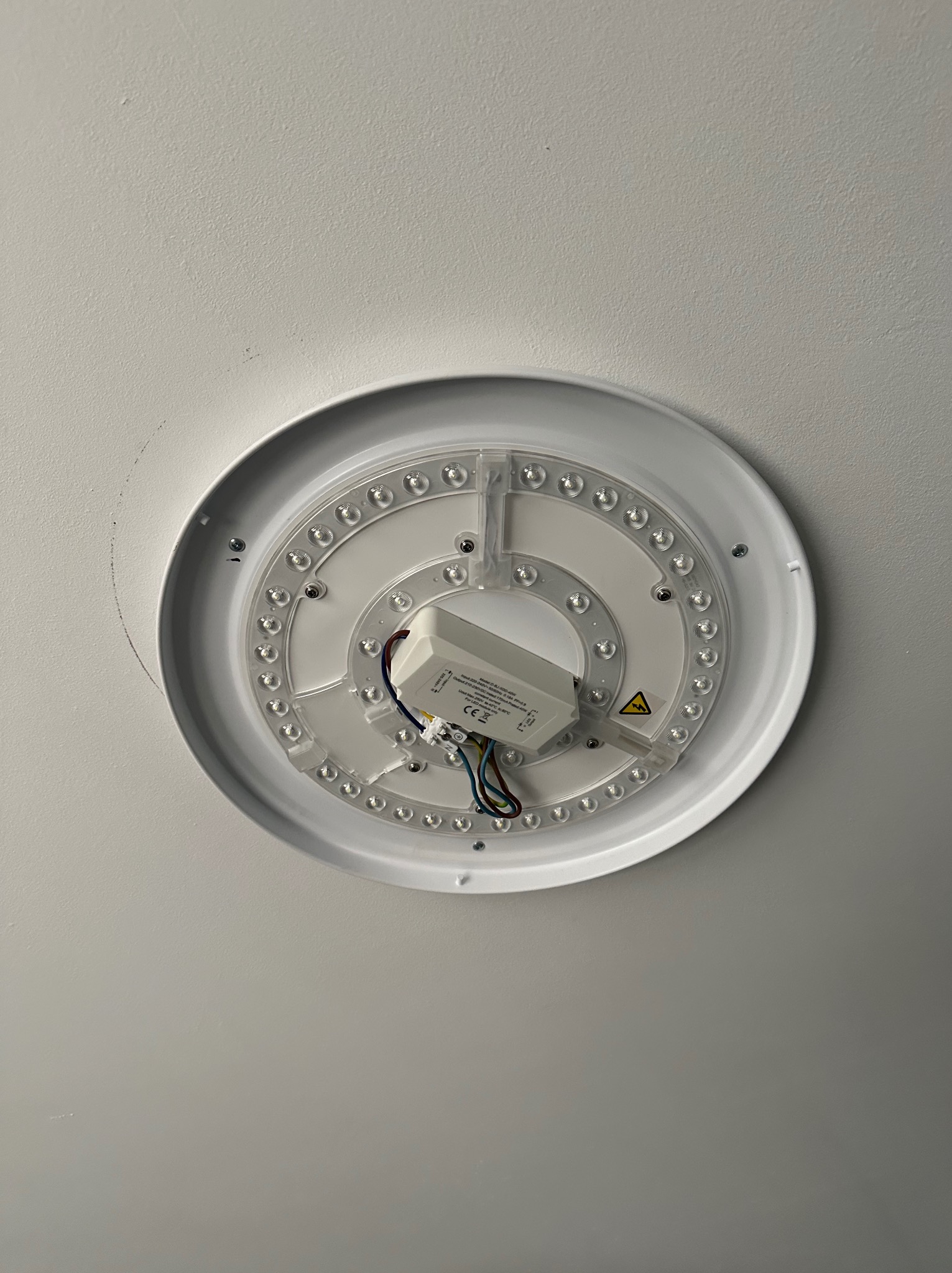 Zamontowana okrągła lampa LED sufitowa z widocznym zasilaczem i okablowaniem na białym suficie. Widok z dołu, oświetlenie wnętrza.