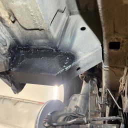 AutoRevive naprawy lakiernicze-blacharskie - Podwozie samochodu po konserwacji antykorozyjnej, widoczne świeżo nałożone, czarne zabezpieczenie na elementach zawieszenia i podwozia. Ujęcie z dołu, w warsztacie.