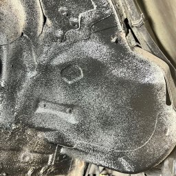 AutoRevive naprawy lakiernicze-blacharskie - Podwozie auta po zabezpieczeniu antykorozyjnym, widoczne elementy zawieszenia i nałożona, czarna powłoka ochronna z białymi drobinkami. Ujęcie z bliska, od dołu.