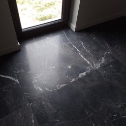 Ciemna, marmurowa podłoga z połyskiem w Nowej Soli, ułożona przy oknie. Widoczne białe żyłki i odbicie światła. Minimalistyczne wykończenie.
