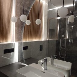 Styl Zakład budowlany Dariusz Stepnowski - Nowoczesna łazienka z podświetlanymi lamelami, marmurowymi płytami i wiszącymi lampami kulami. Umywalka prostokątna z chromowaną baterią. Widoczne gniazdka i szklana kabina prysznicowa.