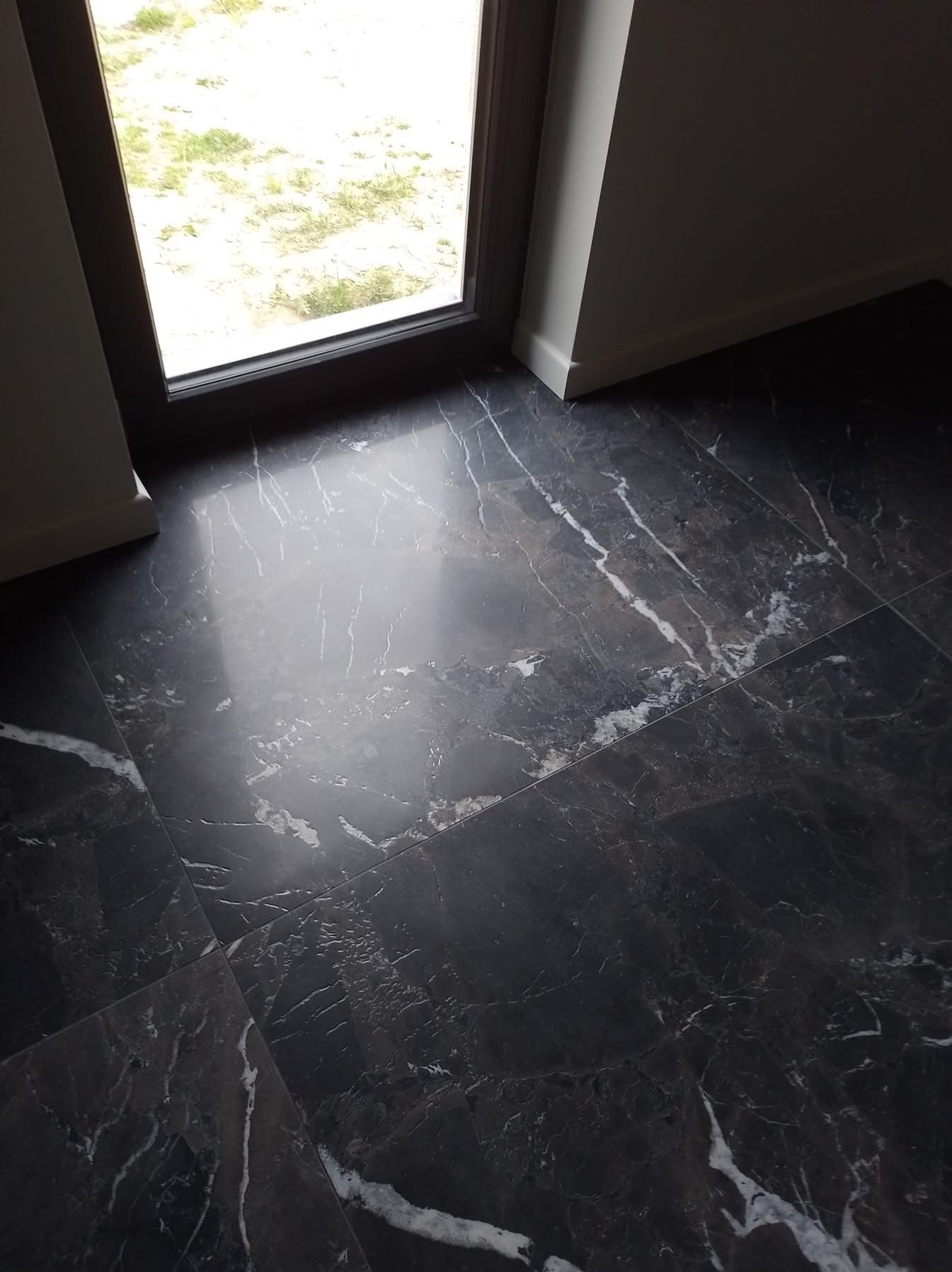 Ciemna, marmurowa podłoga z połyskiem w Nowej Soli, ułożona przy oknie. Widoczne białe żyłki i odbicie światła. Minimalistyczne wykończenie.