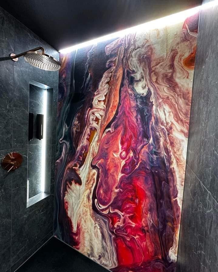 Nowoczesna kabina prysznicowa z panelami dekoracyjnymi imitującymi marmur w odcieniach czerwieni, fioletu i bieli. Widoczna deszczownica i wnęka z oświetleniem.
