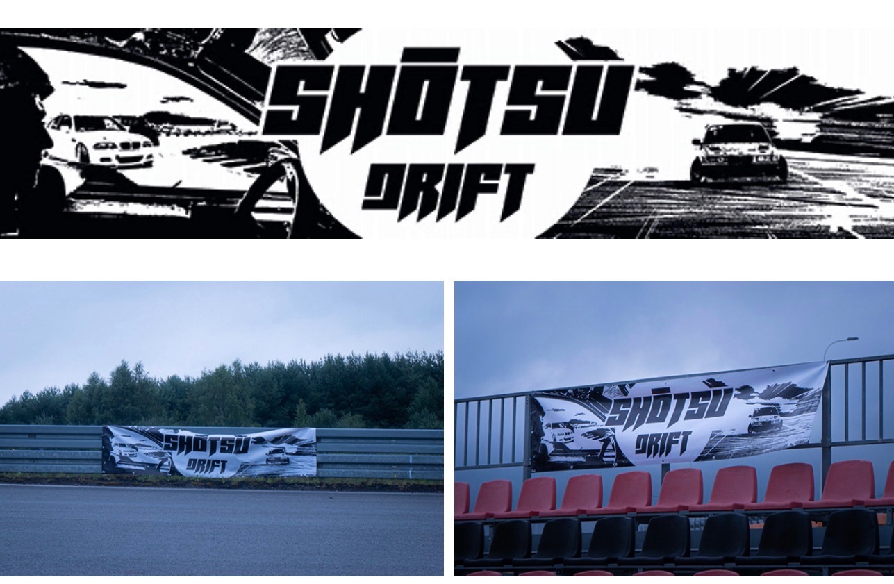 Baner reklamowy z grafiką samochodów driftowych na torze wyścigowym, zamontowany na barierkach i trybunach. Czarno-biała grafika z napisem 'Shotsu Drift'.