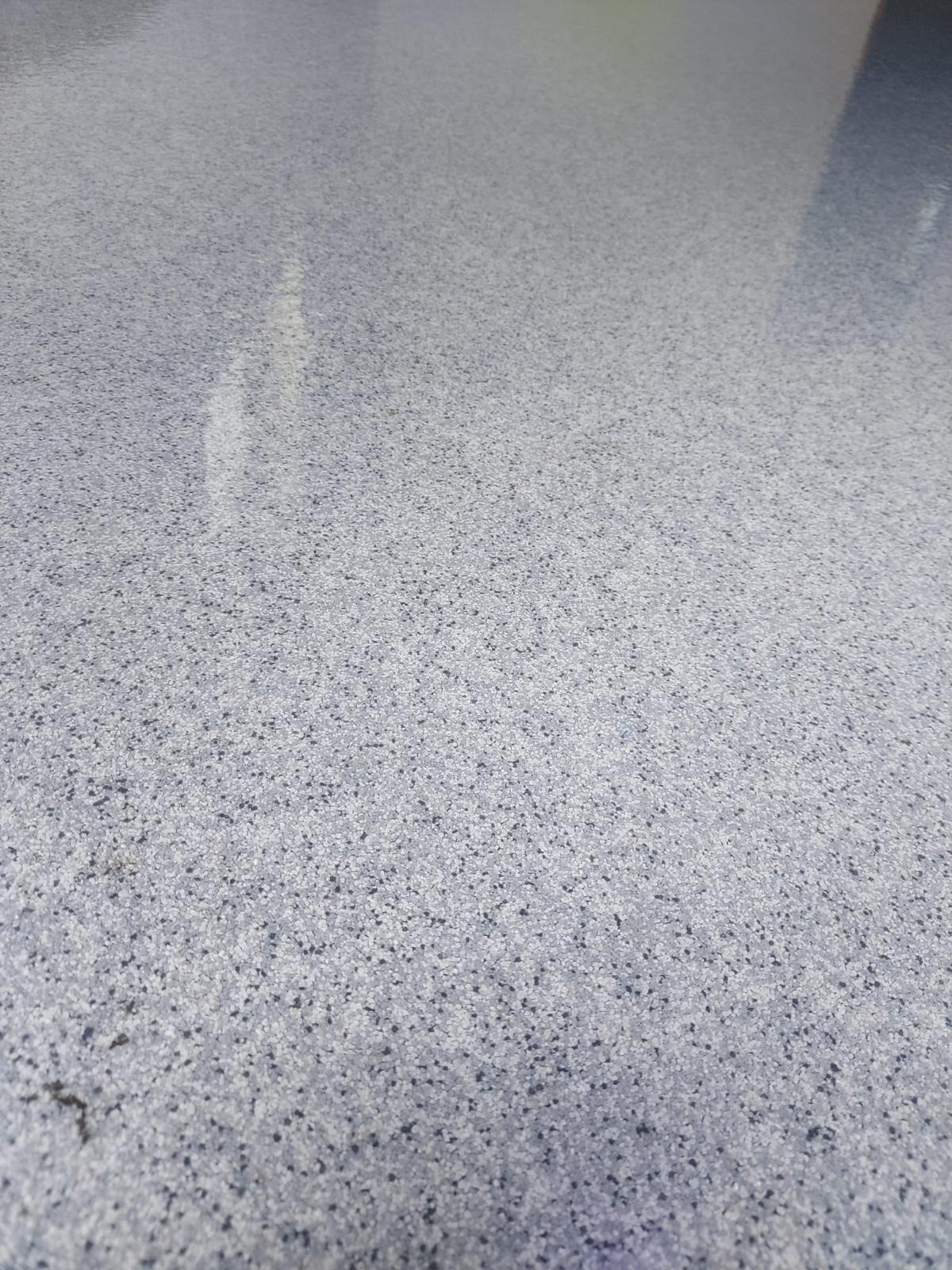 Jasnoszara, gładka powierzchnia z drobnymi, ciemnymi inkluzjami, tworząca jednolitą strukturę. Widoczne delikatne refleksy światła.