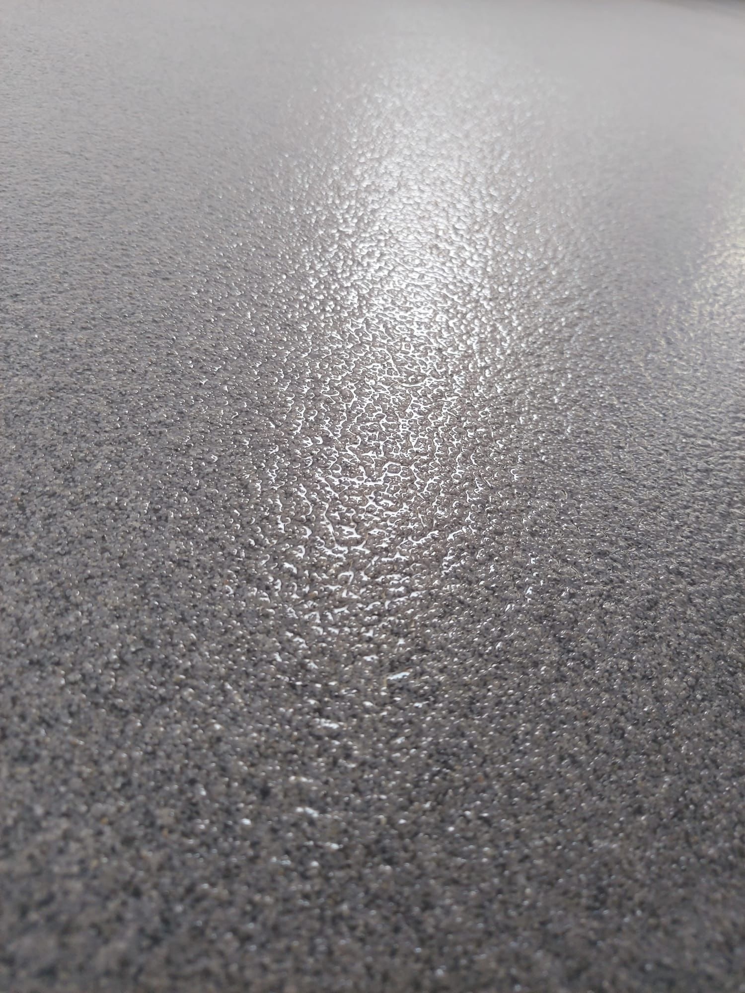Szara, błyszcząca posadzka żywiczna z wyraźną fakturą, oświetlona z góry, ukazana pod kątem. Widoczna struktura powierzchni z bliska.