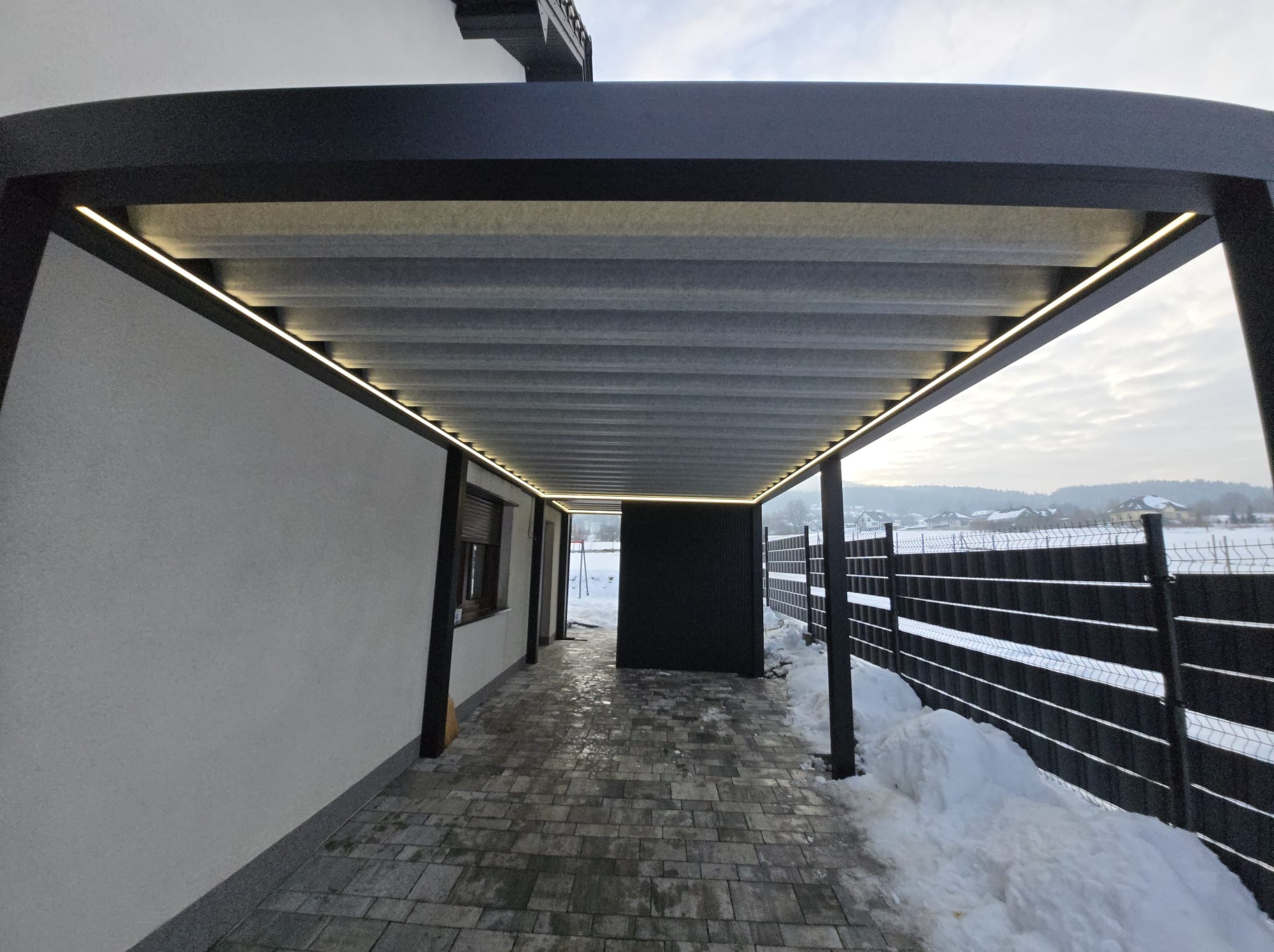 Nowoczesna pergola metalowa z oświetleniem LED, widok z dołu na konstrukcję i otoczenie w zimowej scenerii. Kostka brukowa na podłożu.