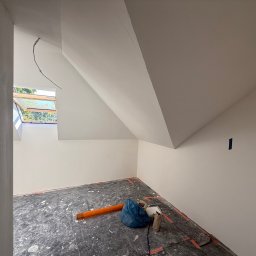 Poddasze po malowaniu na biało, zabezpieczona podłoga folią malarską. Widoczne okno dachowe i fragment instalacji elektrycznej. Świeżo pomalowane ściany i sufit.