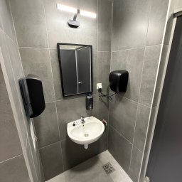 Martin Zawada - Nowoczesna, szara łazienka z umywalką, lustrem i dozownikiem mydła. Minimalistyczny design, płytki imitujące beton, oświetlenie LED. Widoczny odpływ liniowy.