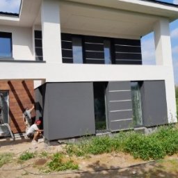 MMBUDMariuszMusinski - Montaż elewacji domu jednorodzinnego z wykorzystaniem paneli drewnopodobnych i grafitowych. Trzech pracowników w trakcie pracy.