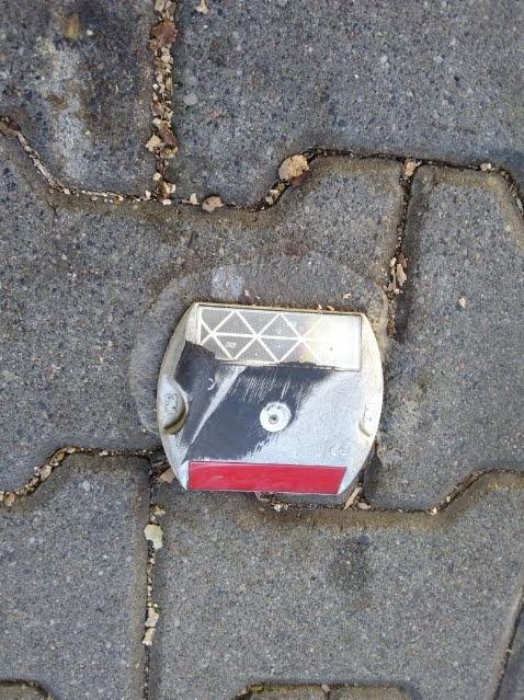 Zamontowany odblask drogowy w kostce brukowej. Widoczne detale montażu i otoczenia. Odblask z elementami odblaskowymi i czerwoną linią.