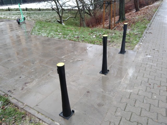 Zamontowane czarne słupki z żółtymi nakładkami na chodniku w Warszawie. Ochrona pieszych i rowerzystów, poprawa bezpieczeństwa ruchu.