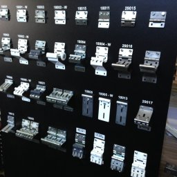 SOLID OKNA - Ekspozycja różnych typów zawiasów do bram garażowych i przemysłowych, zamontowanych na czarnej tablicy z numerami identyfikacyjnymi. Widoczne detale konstrukcyjne.