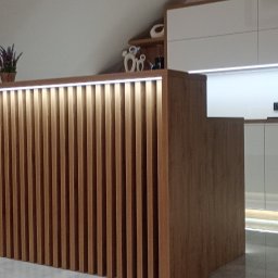 Iskra - Nowoczesna zabudowa kuchenna z drewnianymi lamelami i oświetleniem LED w skosach poddasza. Na blacie doniczki z lawendą, w tle białe szafki i dekoracje.