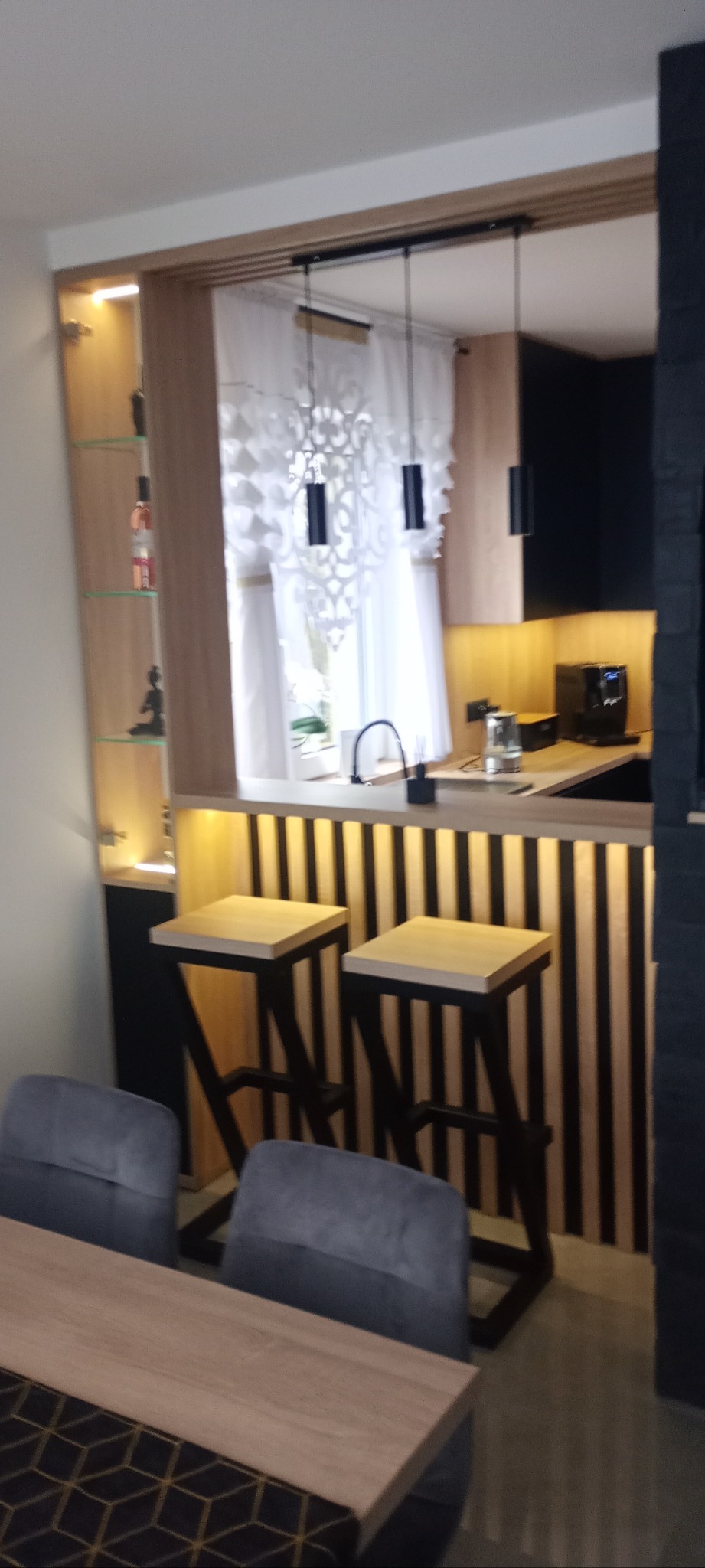 Nowoczesna aranżacja kuchni z barkiem i hokerami w Wieliczce. Zabudowa z oświetleniem LED, czarne akcenty i drewniane wykończenia tworzą spójną całość.