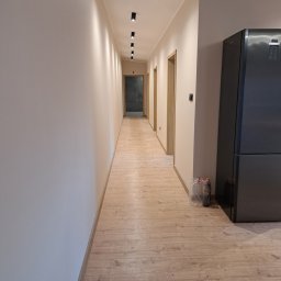 dan-pol - Wykończony korytarz w Wyrzysku z drewnianą podłogą i oświetleniem punktowym. Ściany w jasnym odcieniu beżu. Widoczny fragment lodówki.