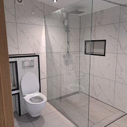 dan-pol - Nowoczesna łazienka z kabiną typu walk-in i podwieszaną toaletą. Białe płytki imitujące marmur z czarnymi akcentami. Minimalistyczny design, szklana ściana kabiny.