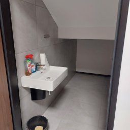 dan-pol - Nowoczesna łazienka z umywalką nablatową, szarą glazurą i skośnym sufitem. Widoczny kosz i środki czystości. Minimalistyczny design, stonowana kolorystyka.