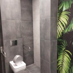 dan-pol - Nowoczesna łazienka z szarymi płytkami, wiszącą toaletą z uchwytami dla niepełnosprawnych i fototapetą z motywem tropikalnych liści.