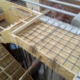 dan-pol - Zbrojenie stropu w szalunku z płyty OSB, widok z góry. Stalowe pręty tworzą siatkę, przygotowane do zalania betonem. Elementy konstrukcyjne budynku w tle.