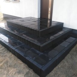 dan-pol - Nowe, czarne schody z kostki brukowej prowadzące do domu, z widoczną fakturą i odbiciami światła na mokrej powierzchni. Ujęcie z dołu, podkreślające solidność wykonania.