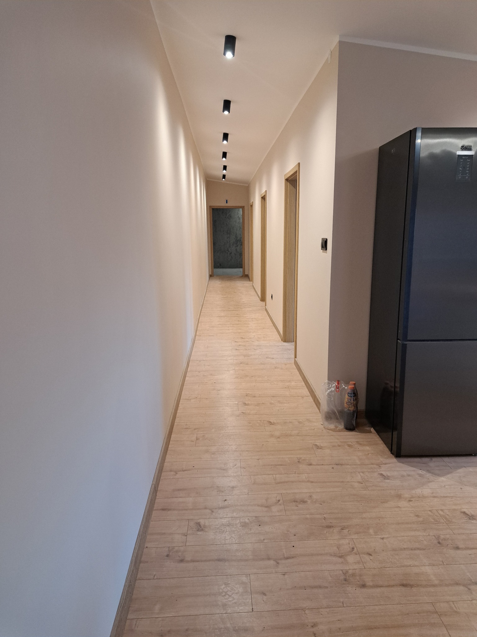 Wykończony korytarz w Wyrzysku z drewnianą podłogą i oświetleniem punktowym. Ściany w jasnym odcieniu beżu. Widoczny fragment lodówki.