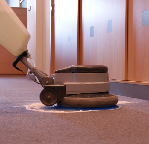 Maszyna czyszcząca wykładzinę w biurze, widoczne ślady czyszczenia i dozownik z płynem.