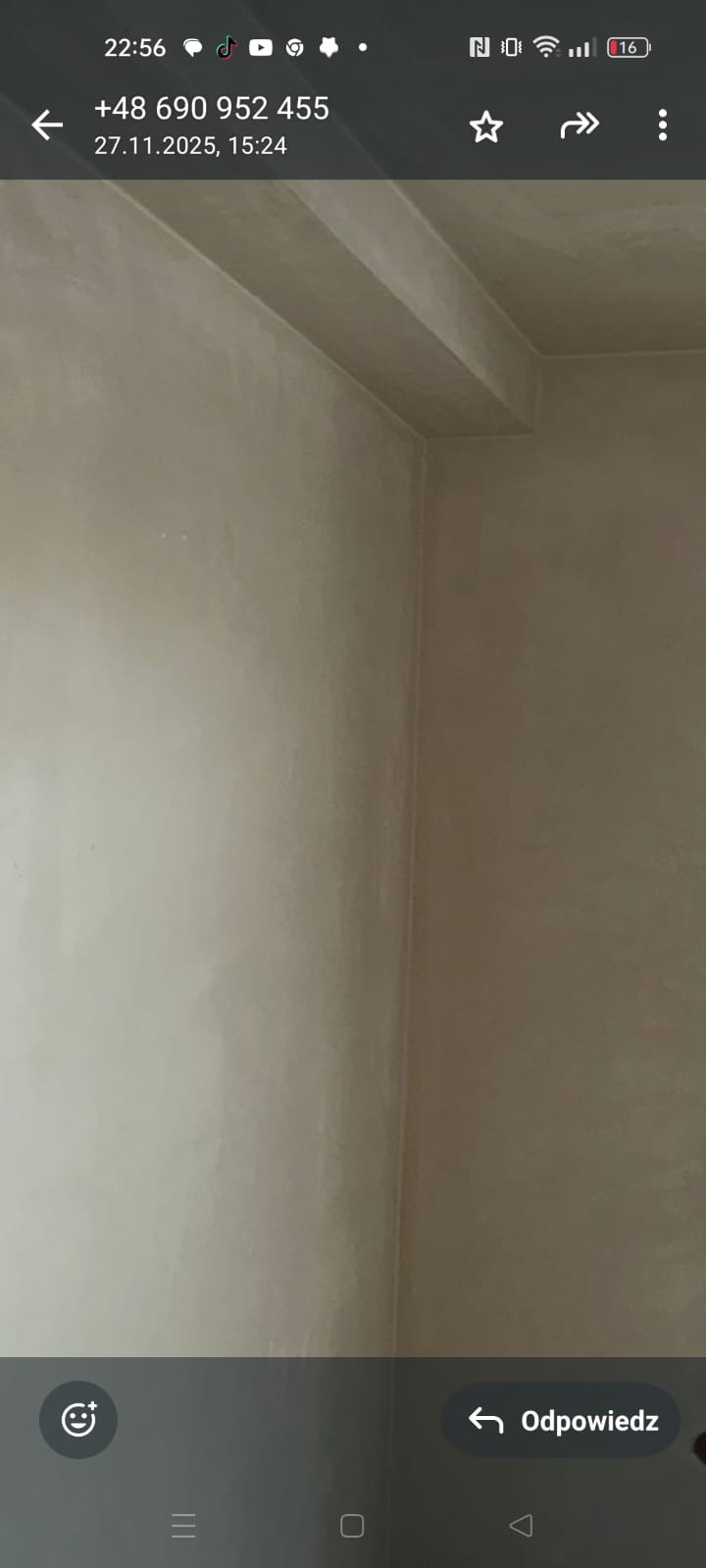 Gładkie, beżowe ściany po nałożeniu tynku w rogu pomieszczenia. Widoczny fragment sufitu z wystającym elementem konstrukcyjnym. Minimalistyczne wykończenie wnętrza.