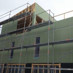 Kacper Smolarczyk - Budowa domu w Piekoszowie. Ściany z płyt OSB, rusztowania. Widoczne otwory okienne i konstrukcja dachu. Etap surowy zamknięty.