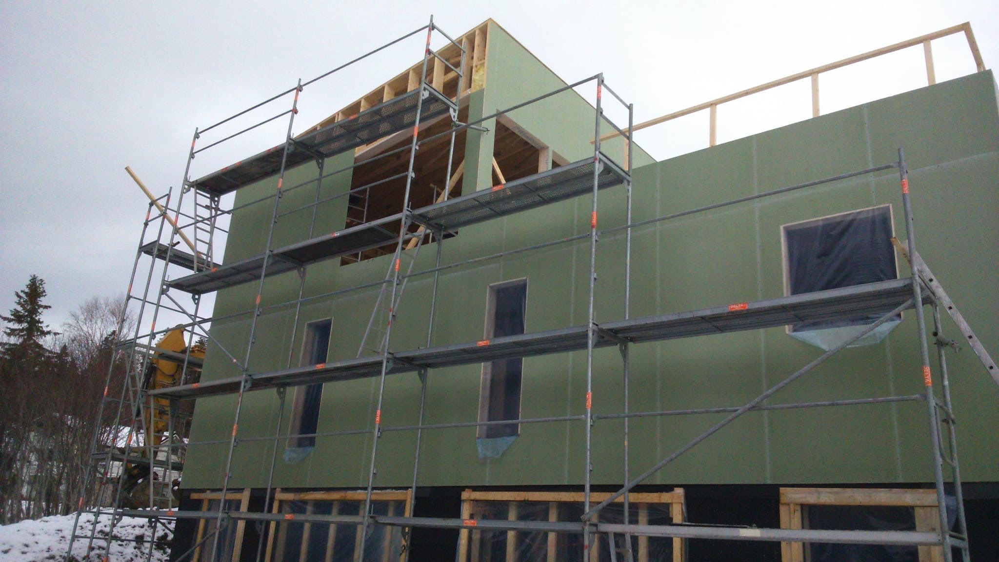 Budowa domu w Piekoszowie. Ściany z płyt OSB, rusztowania. Widoczne otwory okienne i konstrukcja dachu. Etap surowy zamknięty.