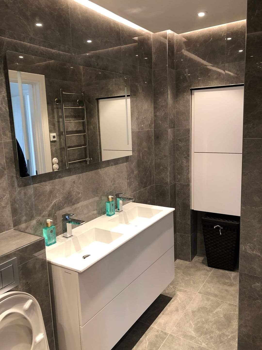 Elegancka łazienka z szarymi płytkami imitującymi marmur, białą podwójną umywalką i szafką, dużym lustrem oraz oświetleniem LED podsufitowym.